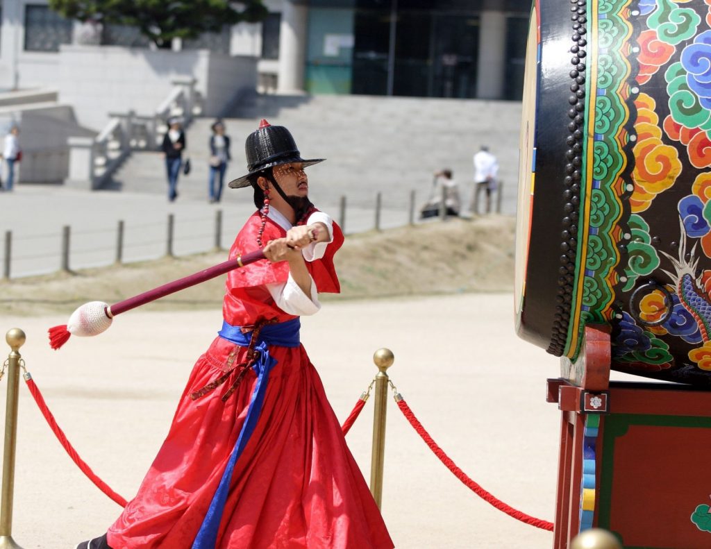 korean-man-in-traditional-costume-beats-the-drum-to-signal-the-changing-of-the-guard-at-kyoungbok-palace-in-Seoul-Korea-1600x1236